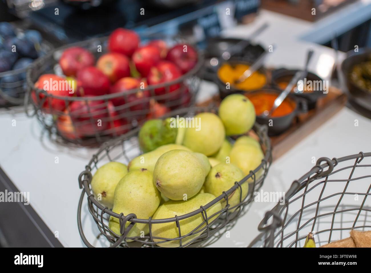 Frische Birnen und rote Äpfel, die in Metallgitterkörben auf einem Hotel-Frühstücksbuffet präsentiert werden. Gesunde Lebensmittelauswahl und Obstauswahl für ein ausgewogenes Stockfoto