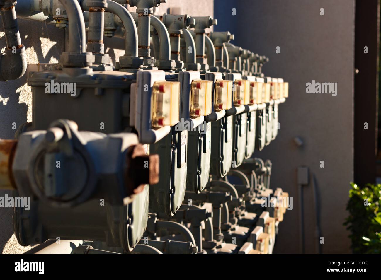 Eine Reihe von Erdgaszählern und miteinander verbundenen Metallrohren, die entlang einer Außenwand des Gebäudes montiert sind. Stockfoto
