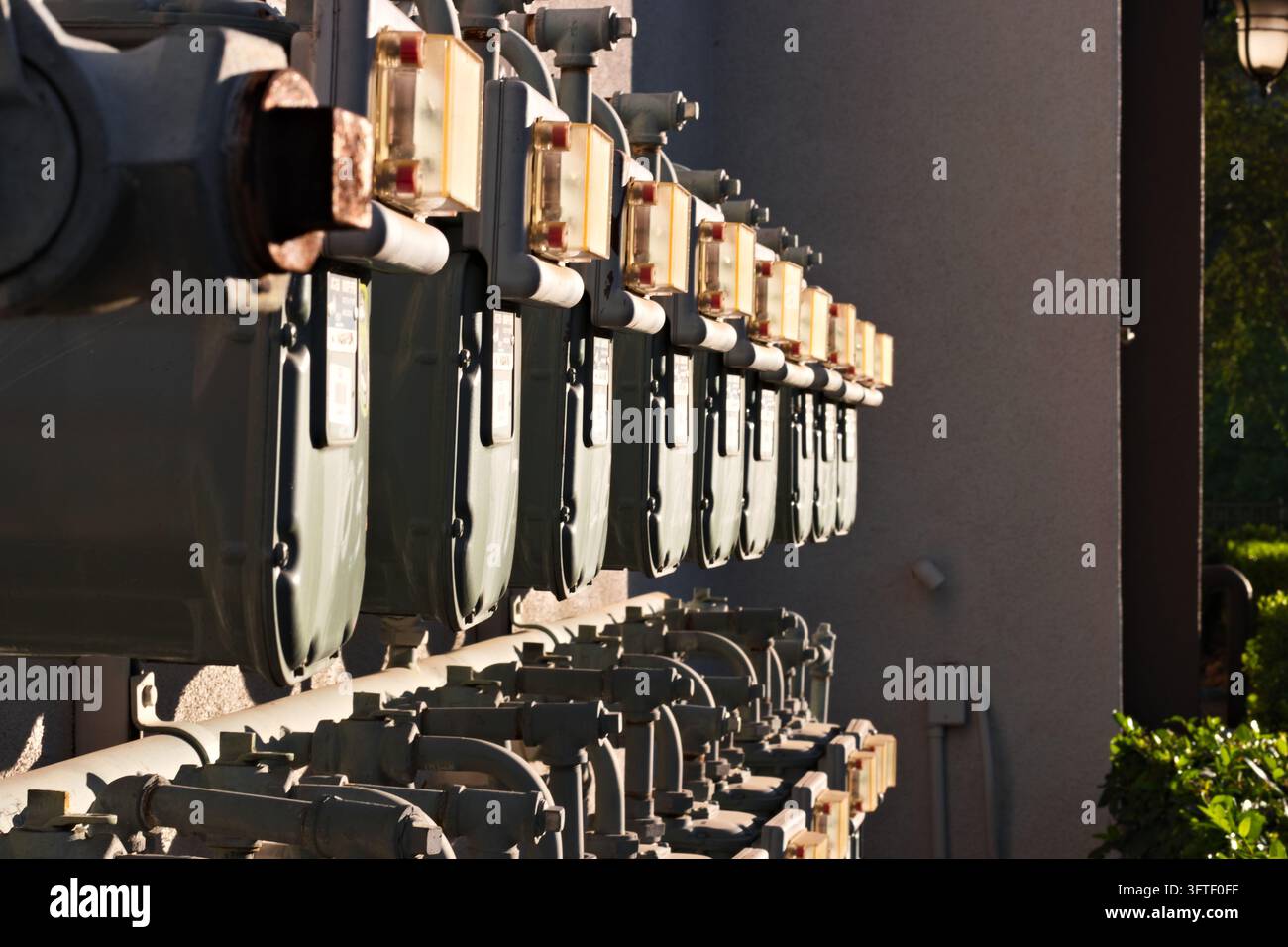 Eine Reihe von Erdgaszählern und miteinander verbundenen Metallrohren, die entlang einer Außenwand des Gebäudes montiert sind. Stockfoto
