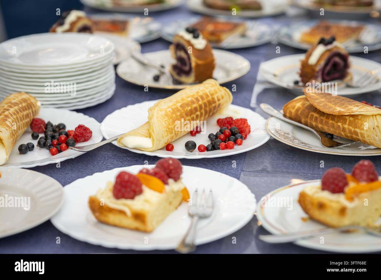 Eine verlockende Auswahl an frisch zubereiteten Waffeln, gerollten Waffelpuffer und verschiedenen Kuchen, die auf weißen Tellern an einem Desserttisch serviert werden. Stockfoto