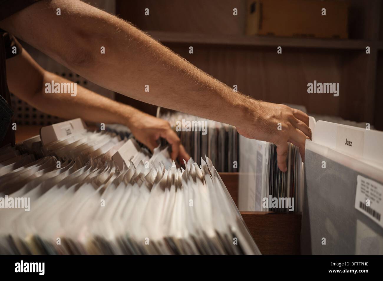 Vinylplatten nach Musikrichtung in einem Plattenladen organisiert, Mann durchstöbert LP-Albenhüllen neben der Jazzabteilung, durchsucht analoge Musiksammlung in hölzernen Ausstellungsregalen. Stockfoto