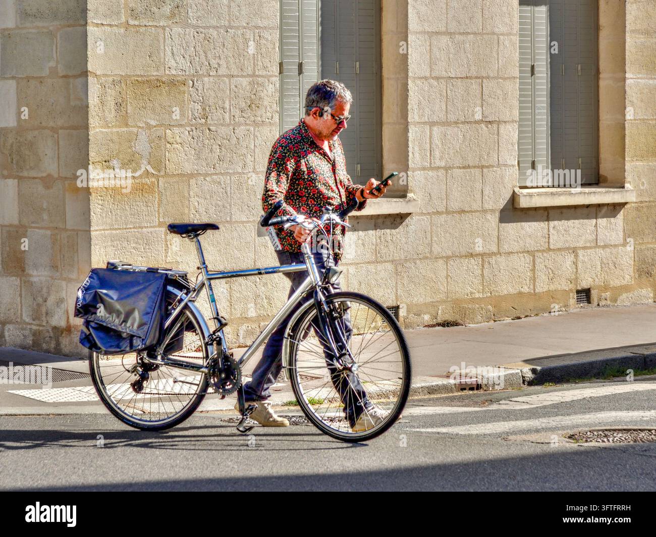 Mann geht neben seinem Fahrrad über eine Innenstadtstraße, während er auf sein Smartphone schaut - Tours, Indre-et-Loire (37), Frankreich. Stockfoto