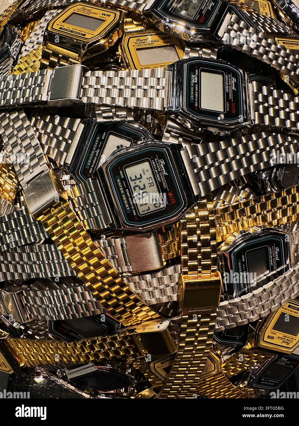 Ein dichter Stapel aus goldenen und silbernen Retro-Digitalarmbanduhren bildet eine zeitgenössische skulpturale Kunstinstallation in der Neuen Nationalgalerie. Stockfoto