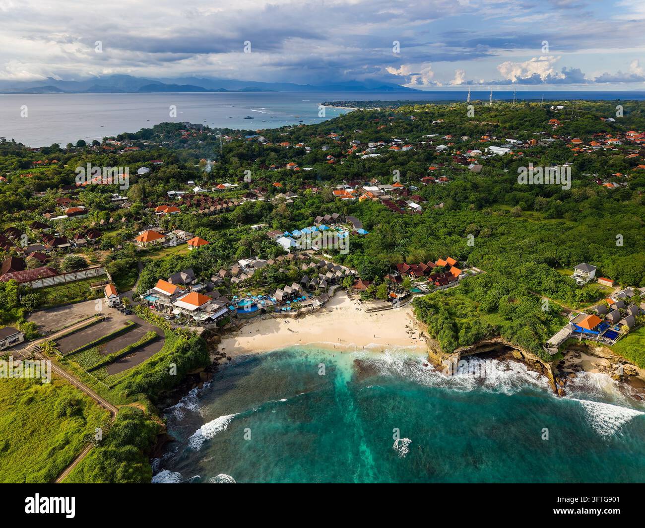 Hohe Luftaufnahme über Dream Beach, türkisfarbene Bucht, die sich zum Bali-Straße öffnet, Küstenresorts und Dorfdächer zwischen üppigen Bäumen Stockfoto