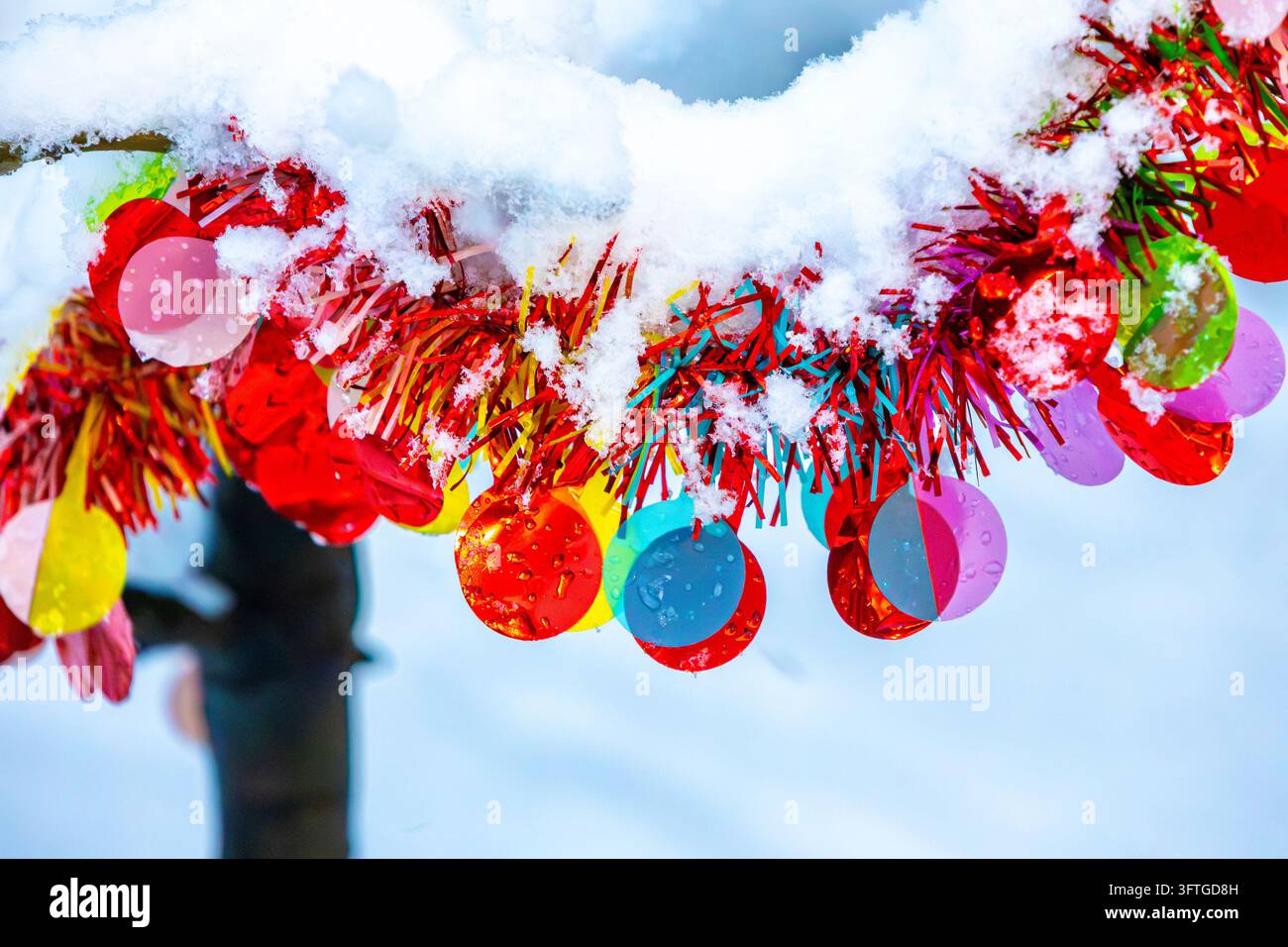 Farbenfrohe glänzende Weihnachtsornamente hängen an einem Baum draußen unter Schnee Stockfoto