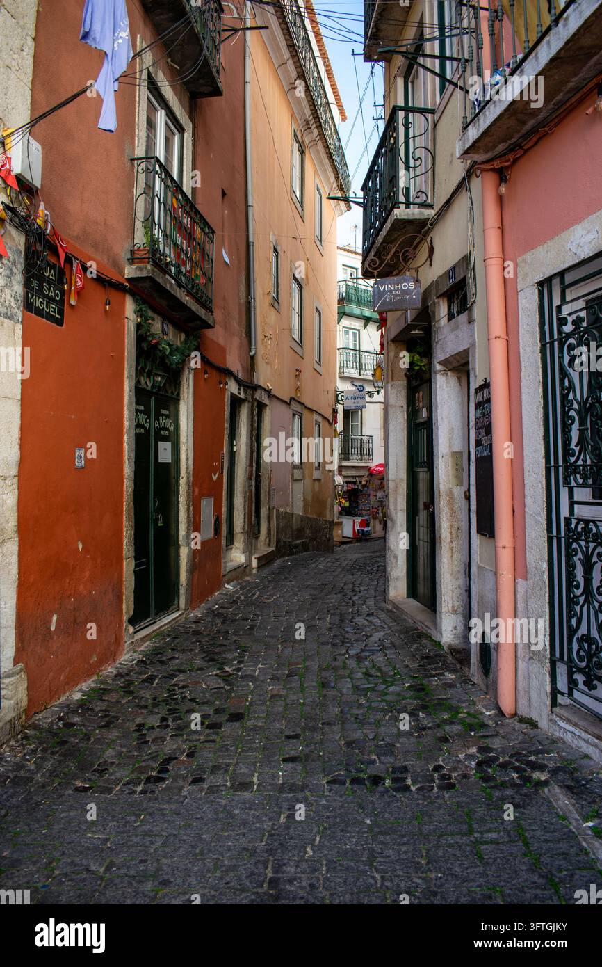 Schmale Kopfsteinpflasterstraße gesäumt von farbenfrohen traditionellen Gebäuden, schmiedeeisernen Balkonen und lokalen Geschäften im historischen Lissabon, Portugal. Stockfoto