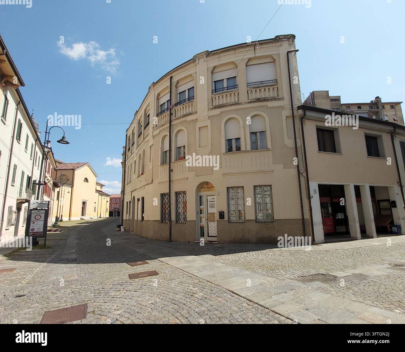 Historisches gebogenes Eckgebäude an einer gepflasterten Straße, die auf die Kirche im Stadtzentrum von Suzzara, Mantua, Lombardei, Italien führt Stockfoto
