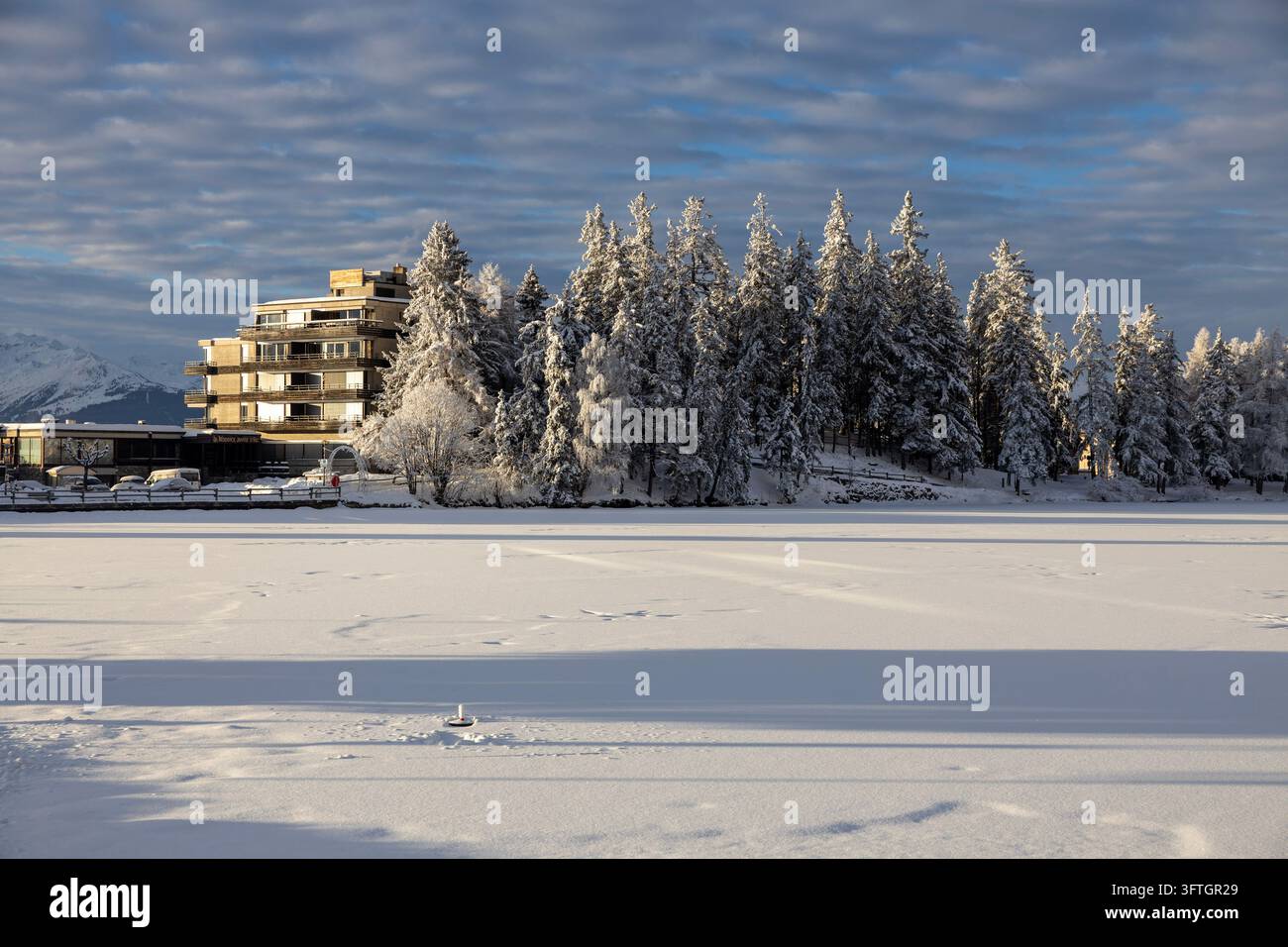 Hotelgebäude zwischen gefrorenen Tannen neben einem schneebedeckten gefrorenen See im Winter, Schweiz Stockfoto