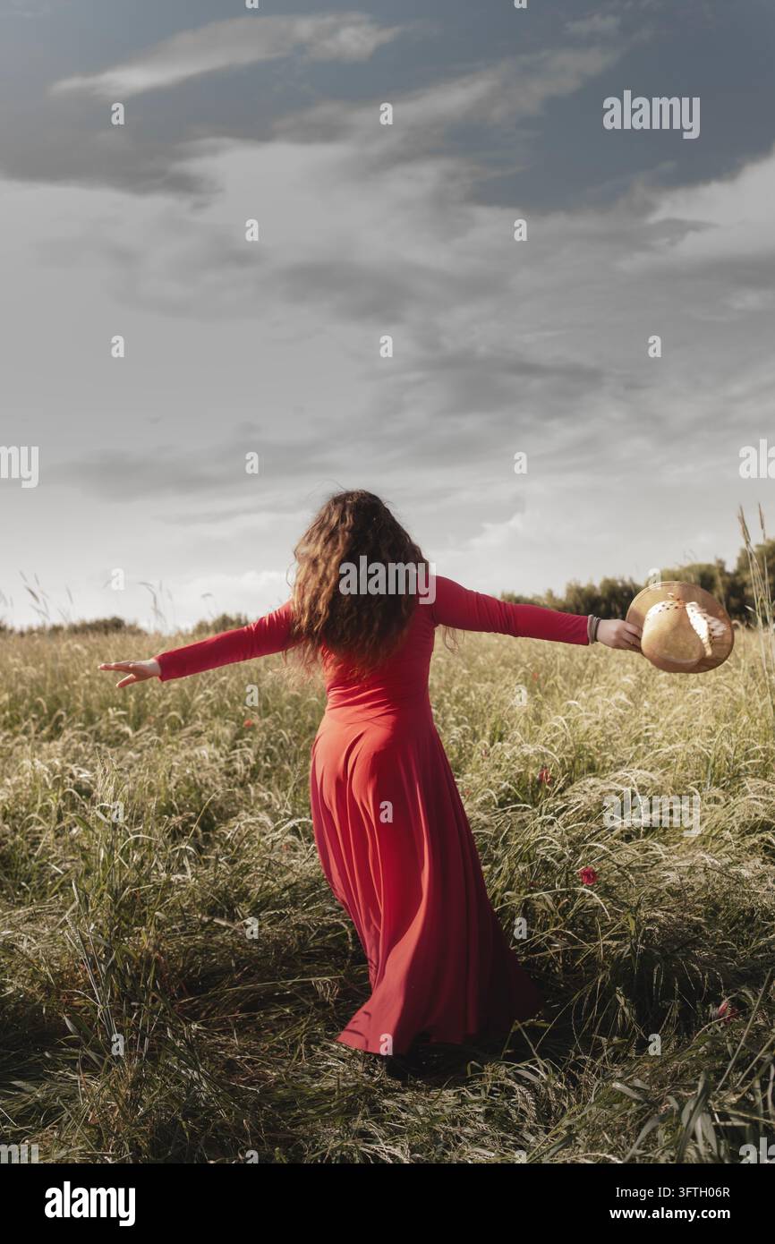 Freiheitsbegeisterte Frau tanzt in der Natur in einem fließenden roten Kleid, das Freiheit und Freude symbolisiert Stockfoto