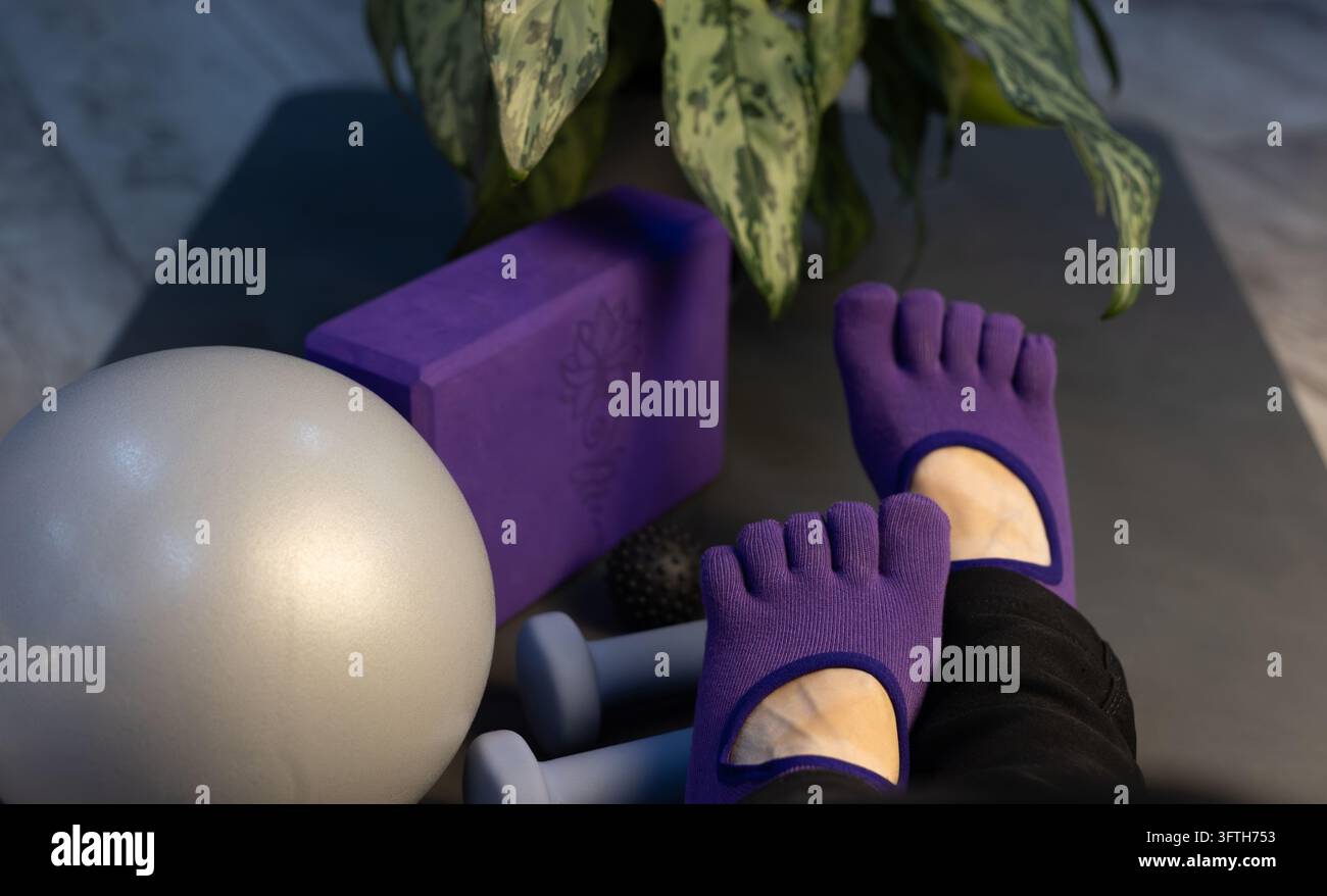 Füße in Yogasocken mit Massageball, Hanteln, Pilatesball und Yoga-Block. Myofasziale Entspannung und Yoga im dunklen Low-Key-Stil Stockfoto