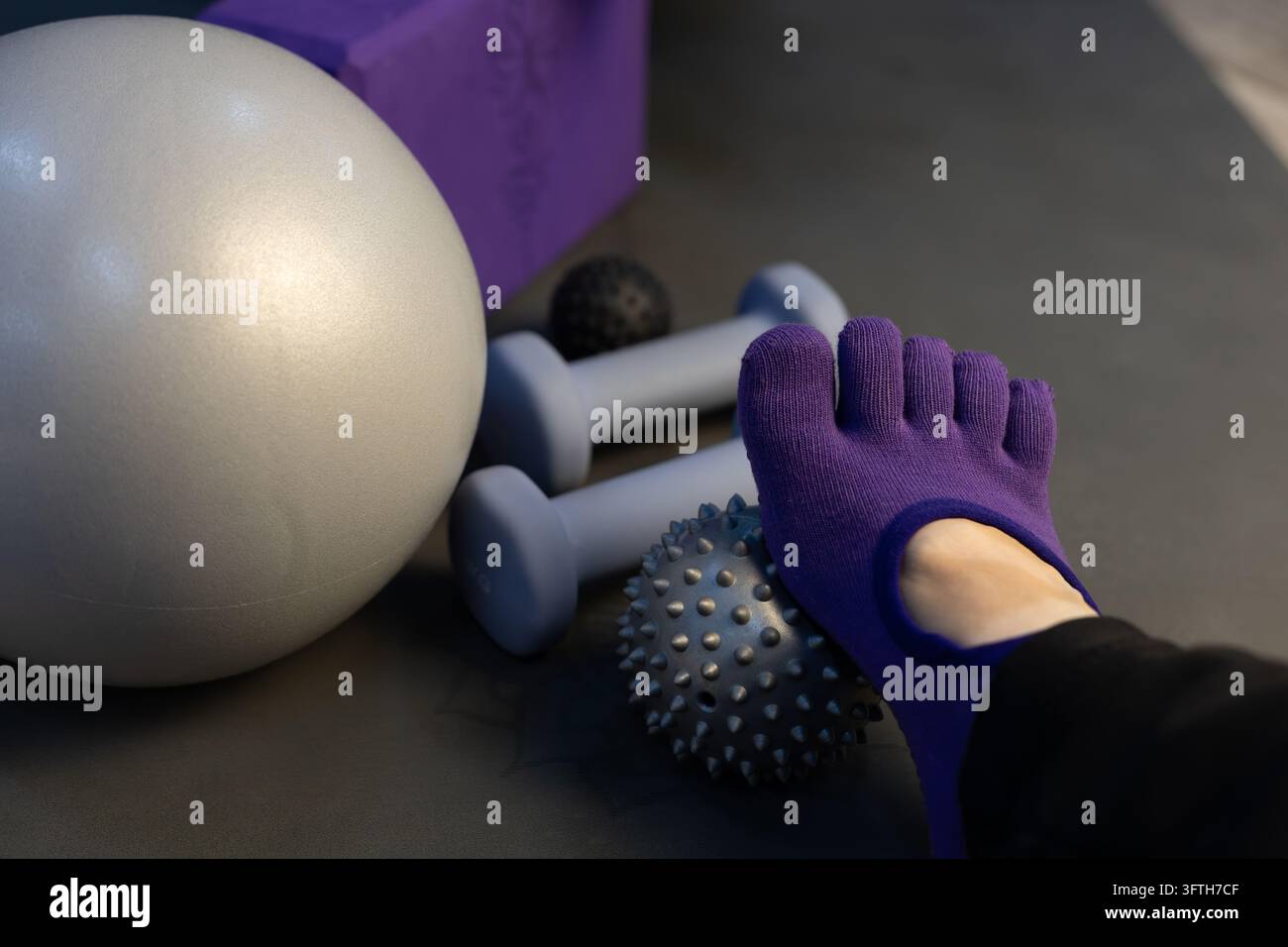 Fuß mit einer Yogasocke mit Massageball, Hanteln, Pilates-Weichball, Yoga-Block. Myofasziale Entspannung und Yoga im dunklen Low-Key-Stil Stockfoto