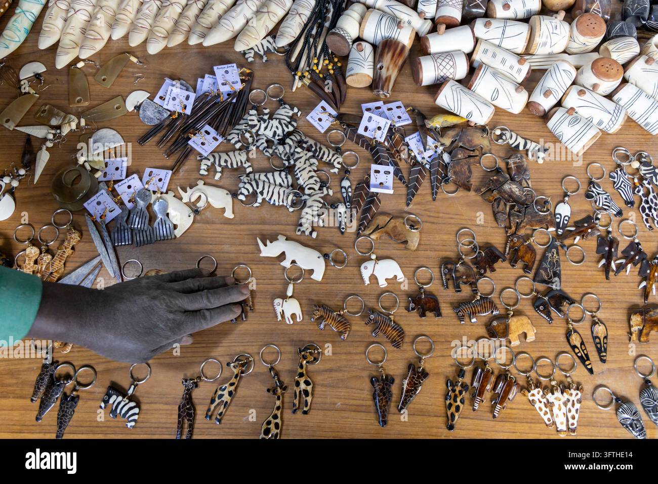 Oberansicht von geschnitzten Knochen-Schlüsselanhängern, Ohrringen und Masken auf einem Holztisch in einer Knochensouvenir-Werkstatt im Kibera-Gebiet, Nairobi County, Nairobi, Kenia Stockfoto