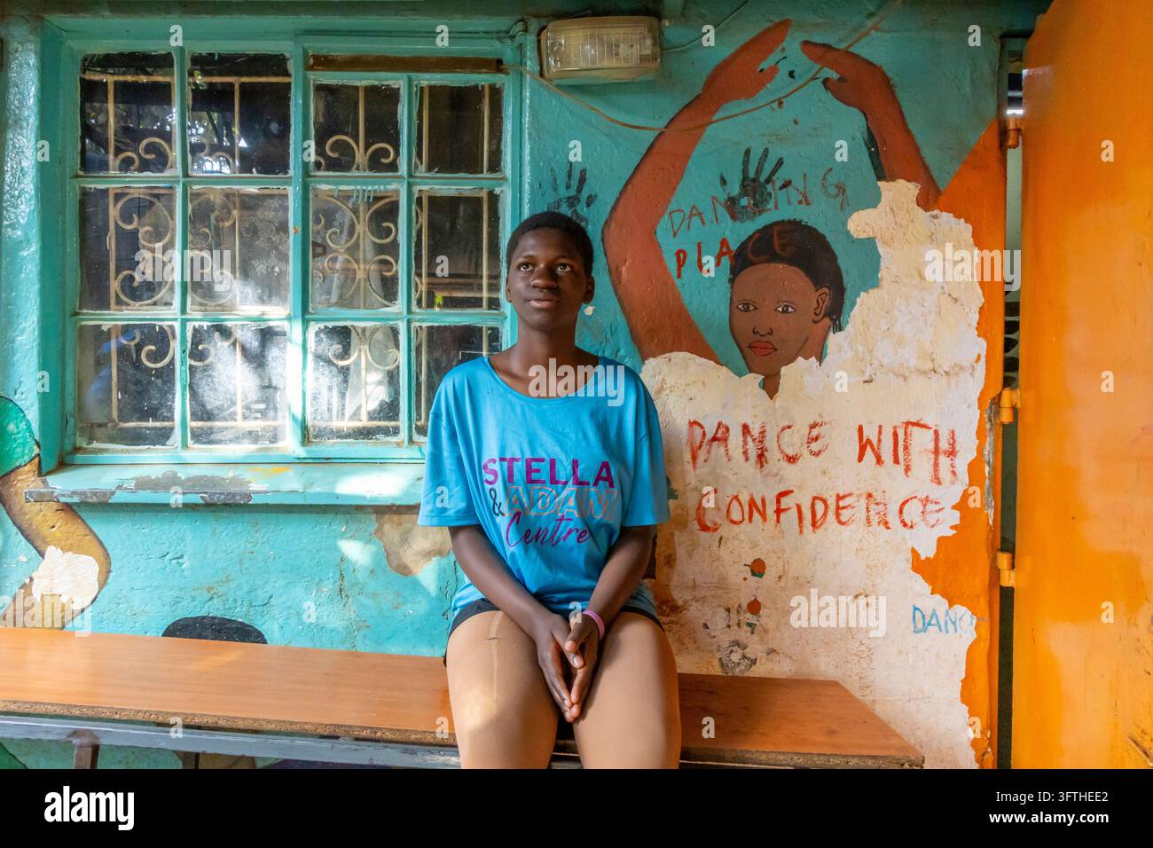 Mädchen in einem Stella and Adam Centre T-Shirt auf einer Bank vor einem "Dance With Confidence"-Mural am Kibera-Ballett, Nairobi County, Nairobi, Kenia Stockfoto