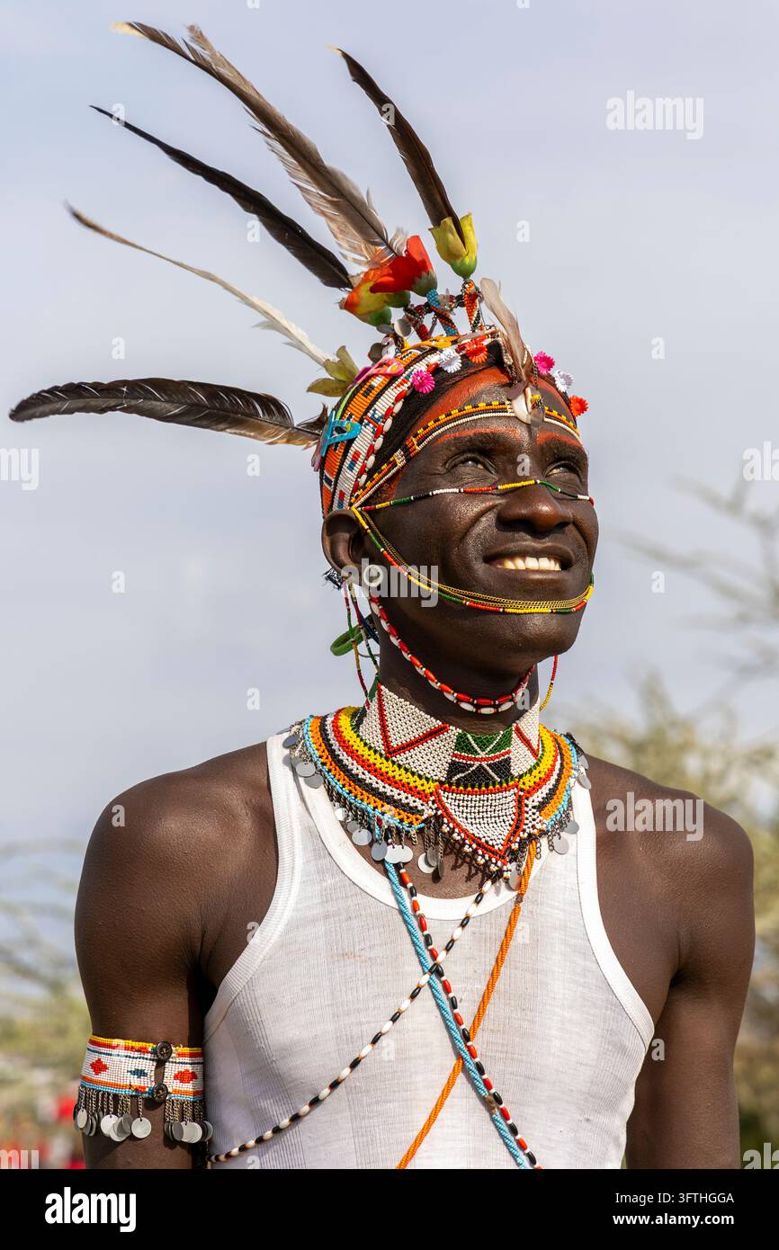 Lächelnder Mann des Rendille-Stammes, der nach oben schaut, mit federndem Kopfschmuck, rotem Gesichtspuder und perlengeschmückten Gesichtsketten, Marsabit County, Loiyangalani, Kenia Stockfoto
