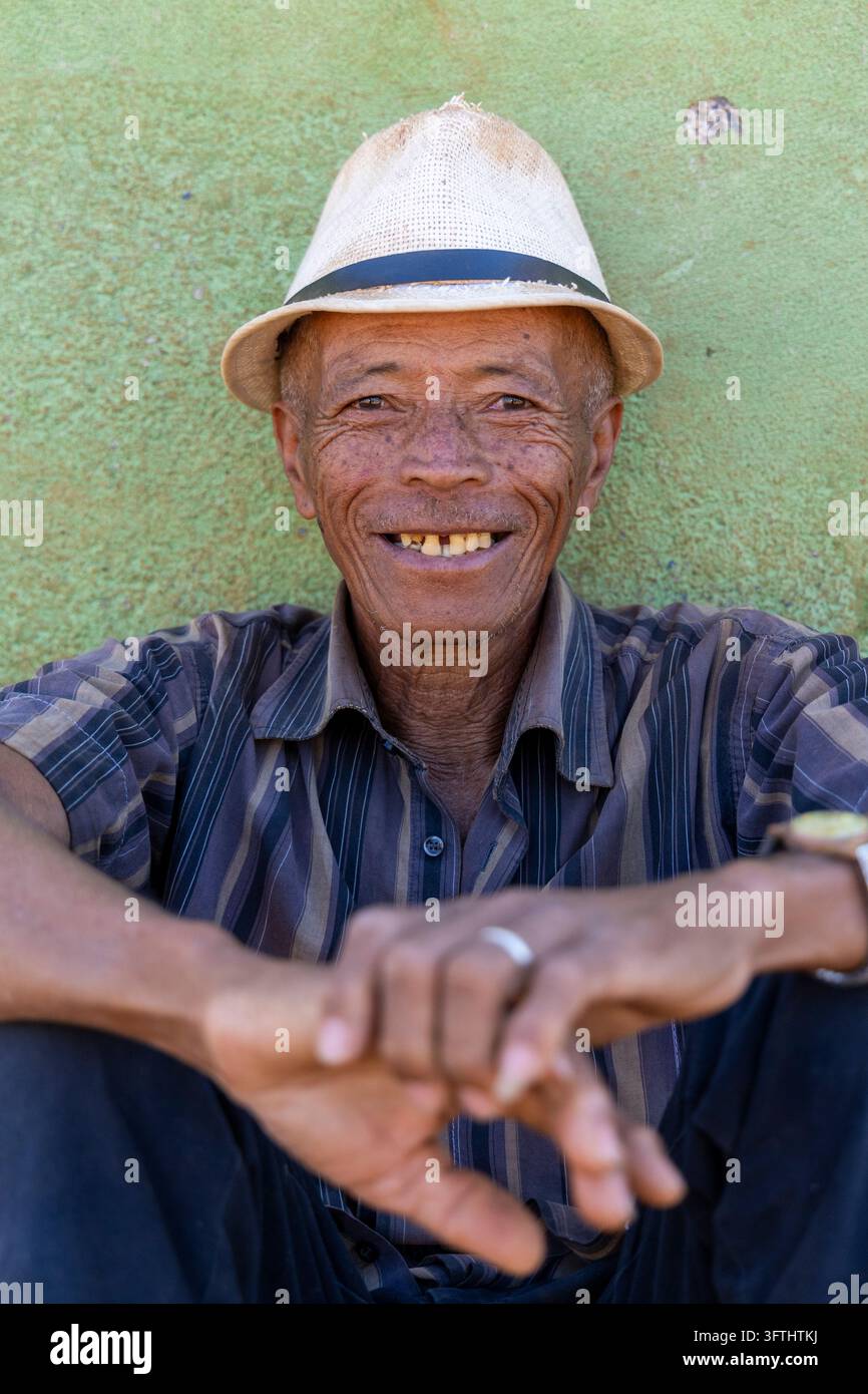 Älterer Mann lächelt, während er einen Strohhut trägt, vor einer grünen Wand, Vakinankaratra, Antsirabe, Madagaskar Stockfoto