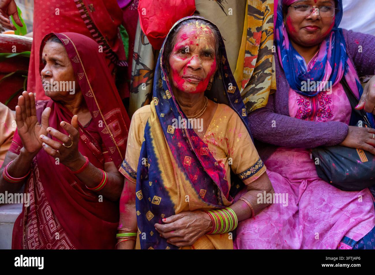 Drei lächelnde ältere Frauen in farbenfrohen Saris und Armreifen mit rosa-rotem und gelbem Puder, Uttar Pradesh, Mathura, Indien Stockfoto