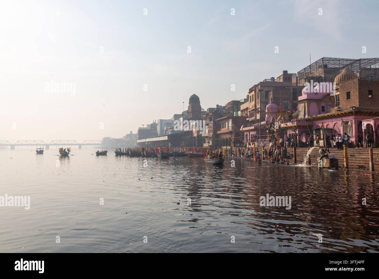Weite Ansicht des Mathura-Ufers mit Booten und Badenden in der Nähe der Ghats und alten Gebäuden entlang des Yamuna-Flusses, Uttar Pradesh, Mathura, Indien Stockfoto