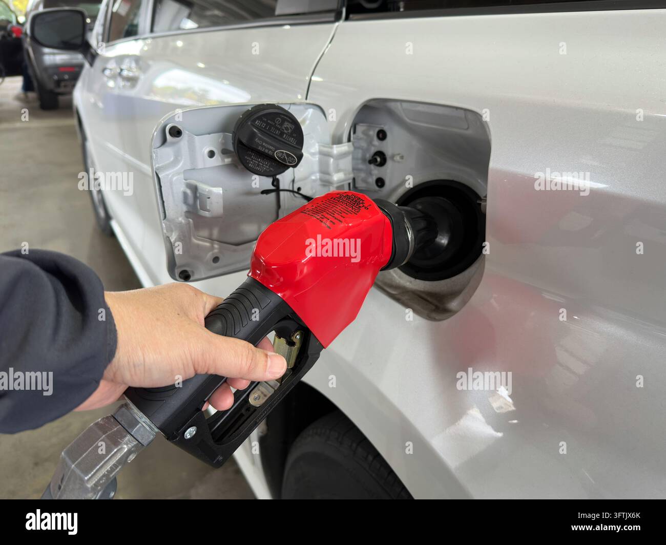 Nahaufnahme einer Person, die einen roten Kraftstoffschlauch in den Tank eines weißen Autos an einer Tankstelle hält. Perfekt für Konzepte rund um Tanken, Fahren und Kraftstoffeffizienz. Stockfoto