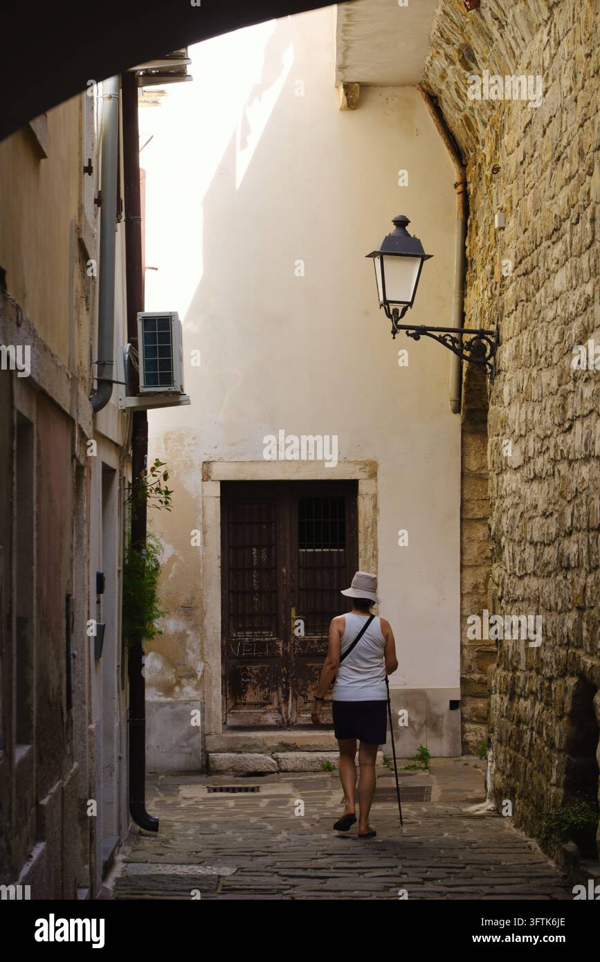 Frau geht durch einen historischen Steinbogen in einer schmalen Kopfsteinpflastergasse in der mittelalterlichen Altstadt von Piran, Slowenien. Stockfoto