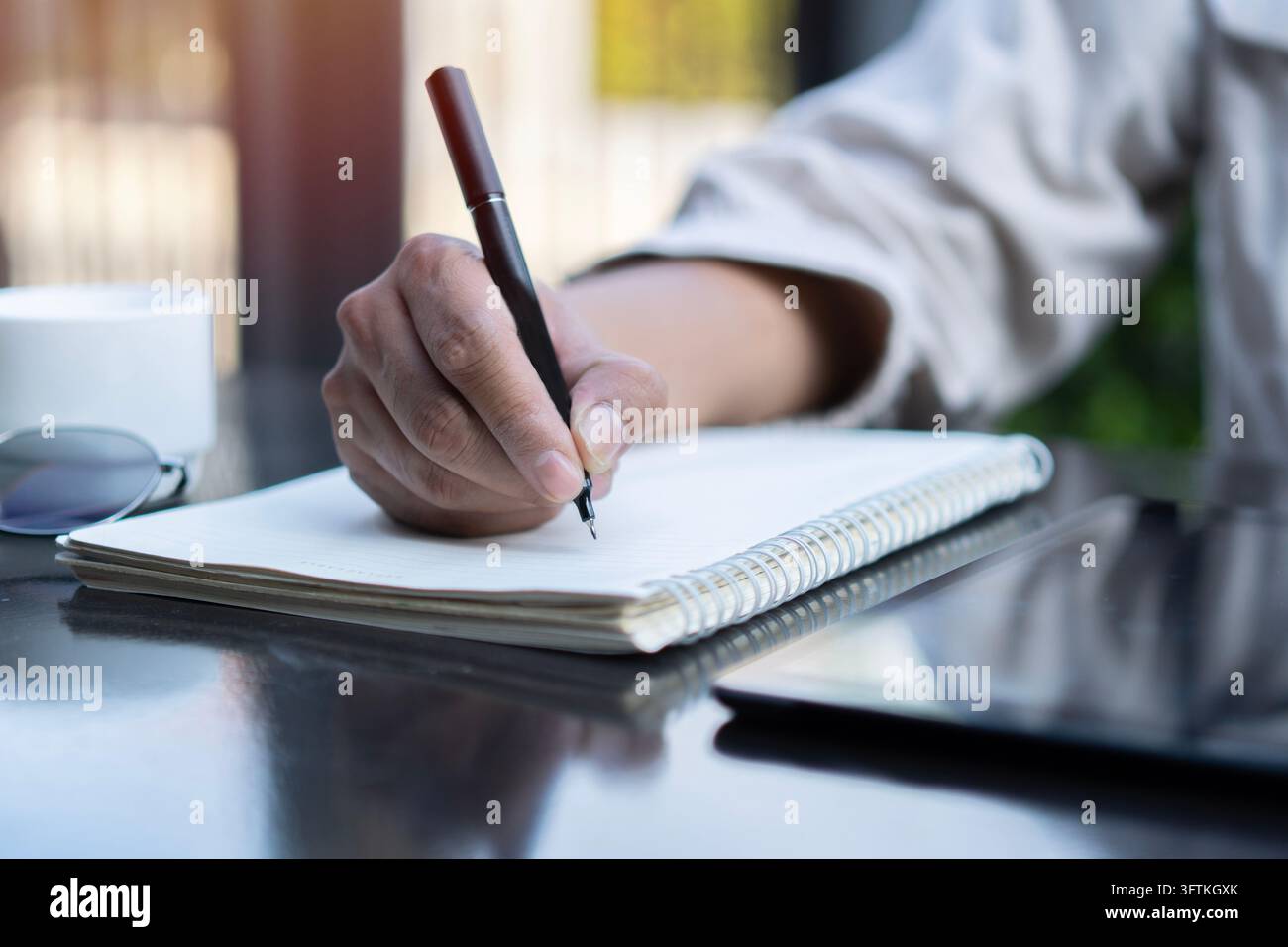 Männerhand mit Stift, die in einem Notizbuch in einem Café schreibt. Mann arbeitet im Freien in einem Café. Nahaufnahme. Platz für Text Stockfoto