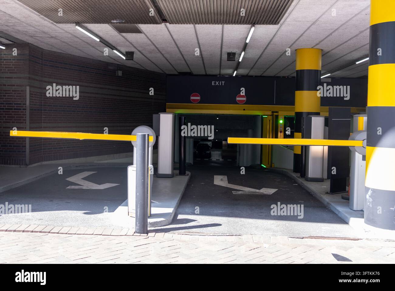 Gelbe Schrankenarme kontrollieren den Ein- und Ausfahrt zu einer Tiefgarage, mit gestreiften Säulen, Pfeilen, hartem Mittagslicht, Niederlande. Stockfoto