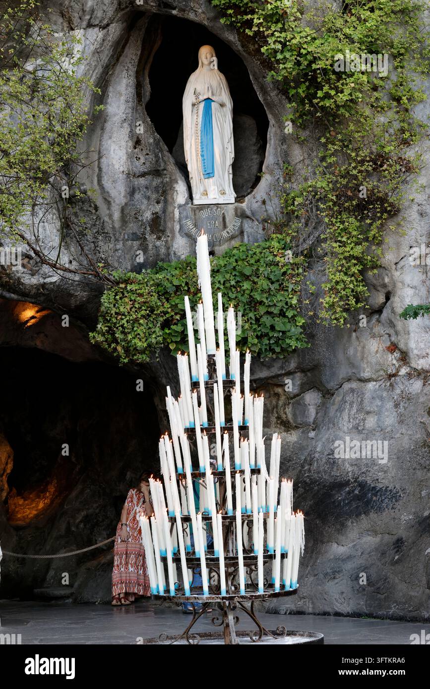 Ein Kandelaber mit brennenden Kerzen vor der Massabielle-Grotte, mit der Statue der Jungfrau Maria in ihrer Nische. Lourdes, Frankreich. Stockfoto