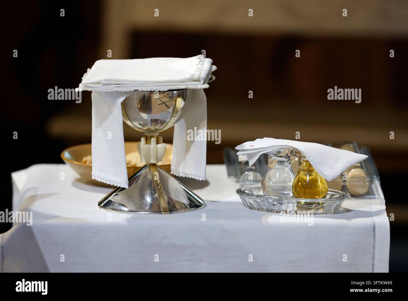 Details eines für eine katholische Messe aufgestellten Altars, mit einem mit liturgischen Tüchern bedeckten Kelch, einer Patene und Kruhen mit Wein, Wasser und Öl. Stockfoto