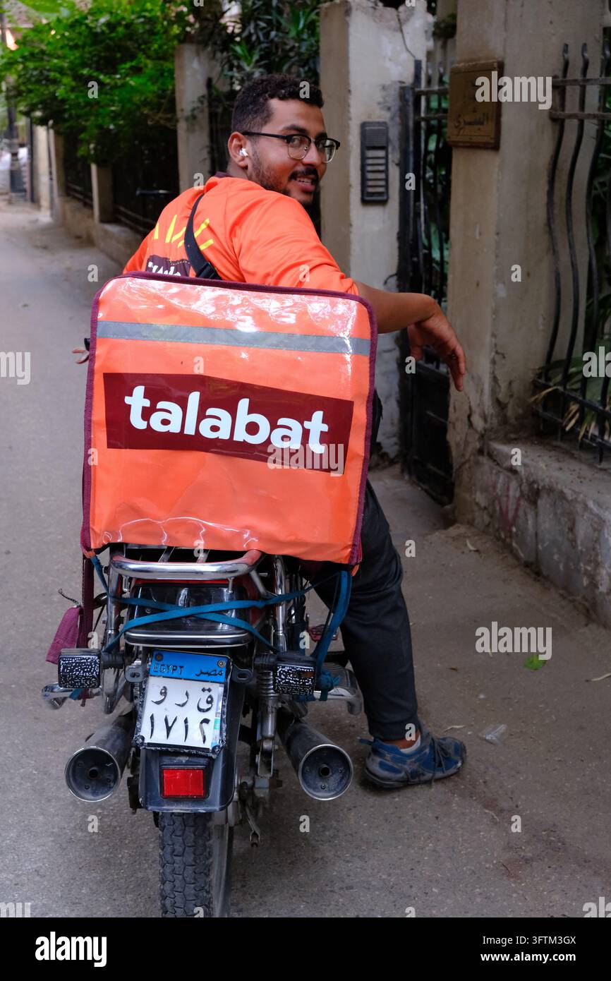 Ein lächelnder Lieferfahrer von Talabat fährt mit seinem Motorrad eine Gasse in Kairo, Ägypten, hinunter. Stockfoto