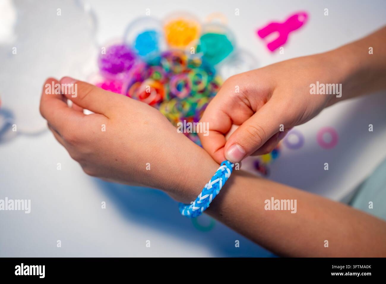 Kind legt ein selbstgemachtes blaues Gummiband-Armband nach dem Weben am Handgelenk an. DIY-Schmuckherstellung fördert Kreativität, Feinmotorik und ein Gefühl von Stockfoto