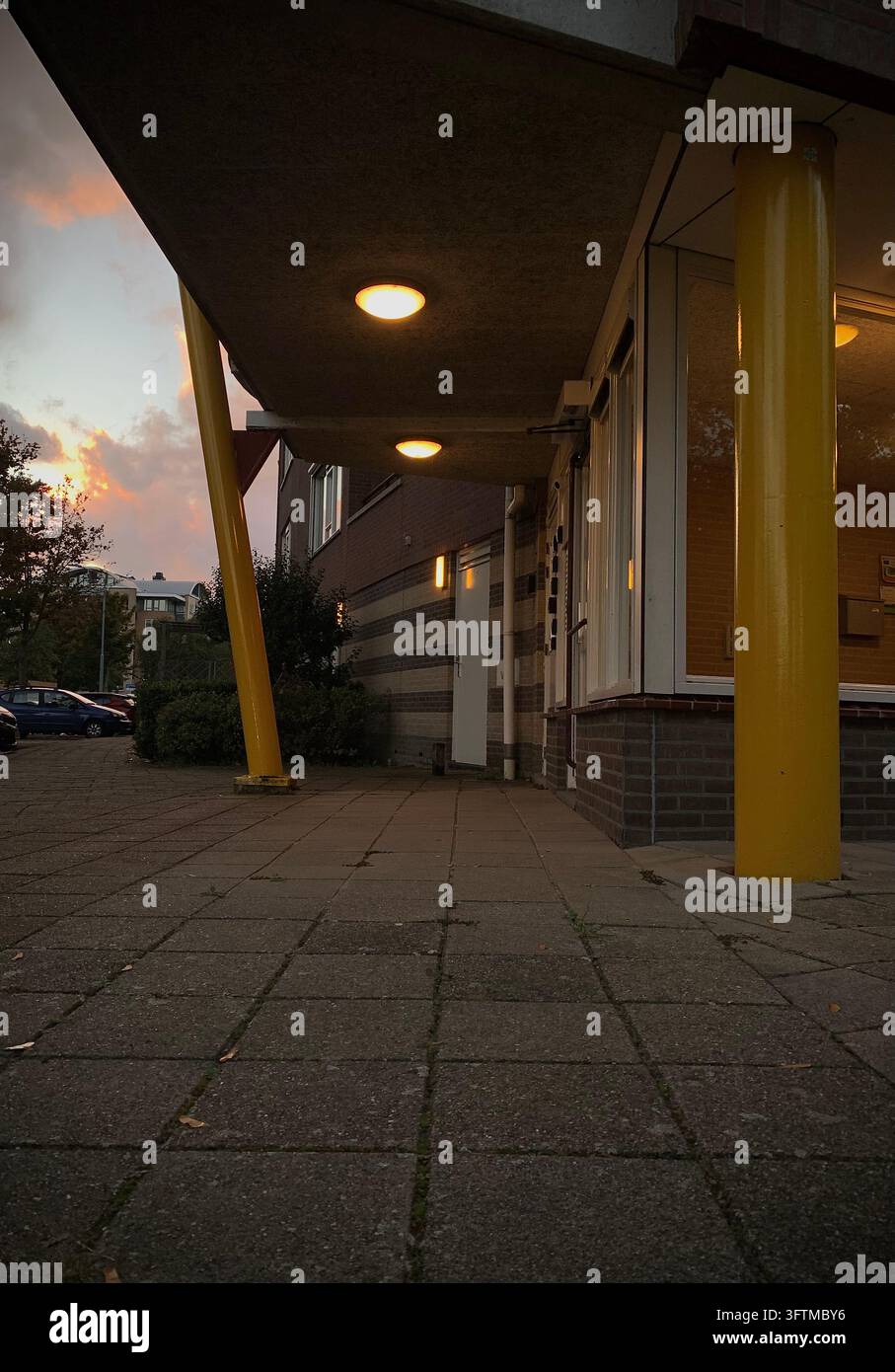 Moderner Gebäudeeingang bei Sonnenuntergang mit hellgelben Säulen und Deckenleuchten. Stockfoto