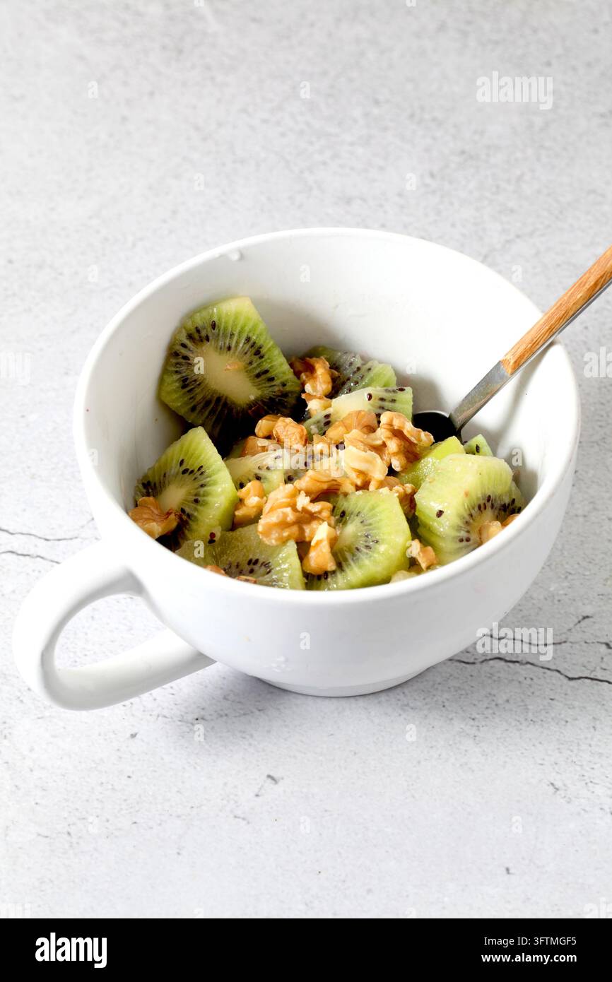Weiße Schale mit gehacktem Kiwi und Walnüssen, von oben gesehen Stockfoto