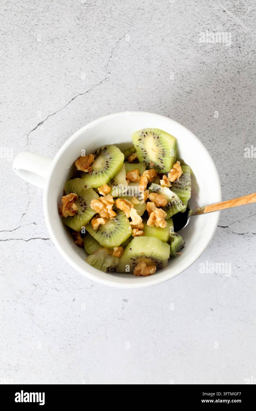 Weiße Schale mit gehacktem Kiwi und Walnüssen, von oben gesehen Stockfoto