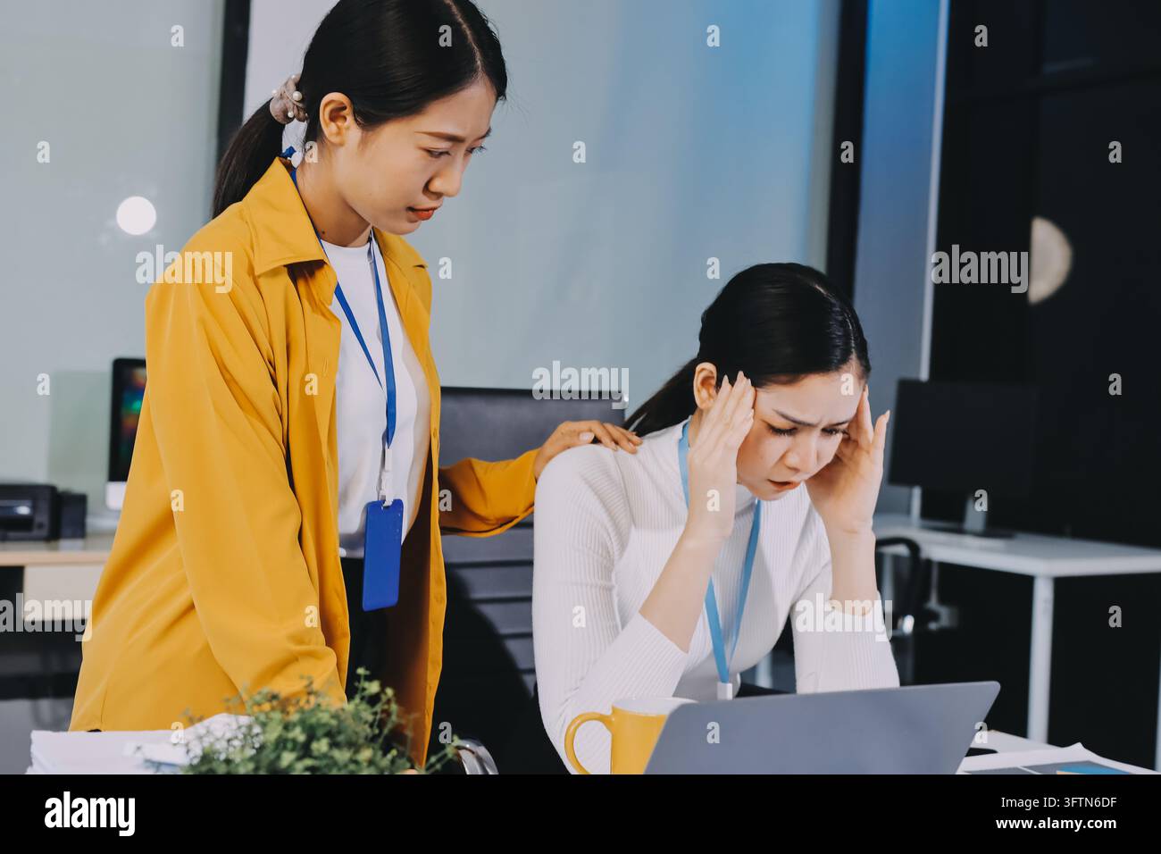 Zwei asiatische Geschäftsfrauen stehen im Büro unter Stress und Kopfschmerzen, fühlen sich durch den Arbeitsdruck erschöpft und konzentrieren sich auf psychische Gesundheit und Stressmanagement Stockfoto