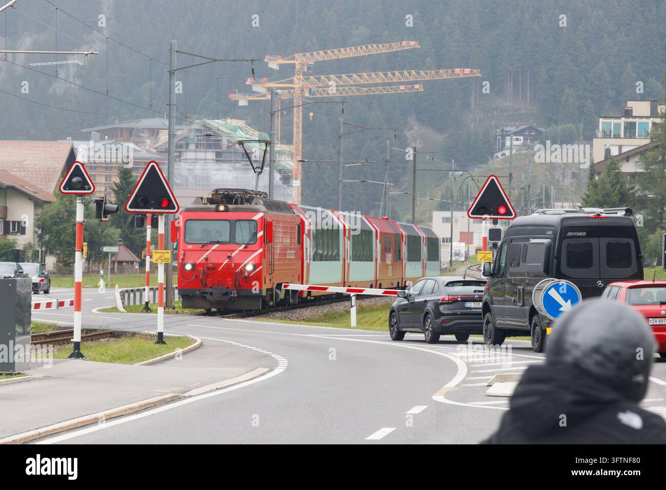 Roter Matterhorn Gotthard Bahn-Zug überquert die Straße an einem Bahnübergang in der Schweiz mit Autos, die an der Schranke warten Stockfoto
