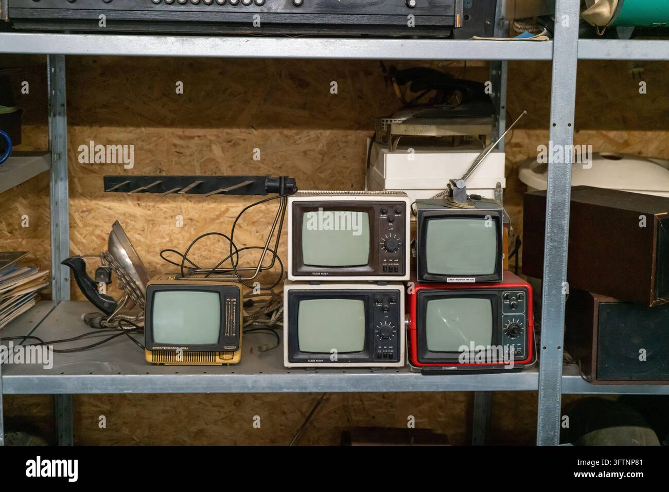 Gestapelte Vintage-Fernseher und Retro-Fernsehgeräte auf Metallregal in überfülltem Lagerraum Stockfoto