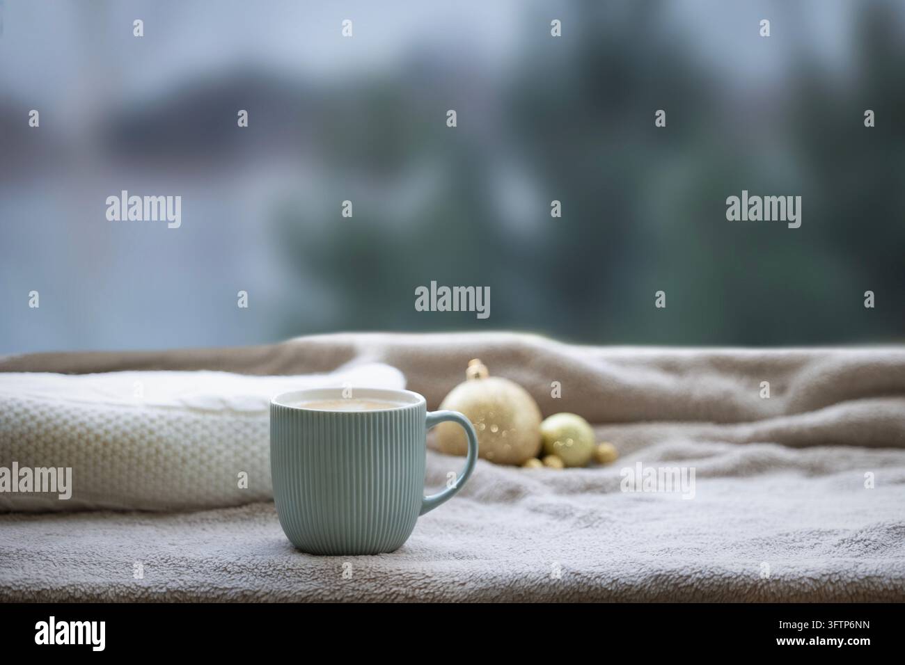 Gemütliche Winter-Stillleben mit mintgrüner Tasse, weicher beiger Decke und goldenen Verzierungen Stockfoto