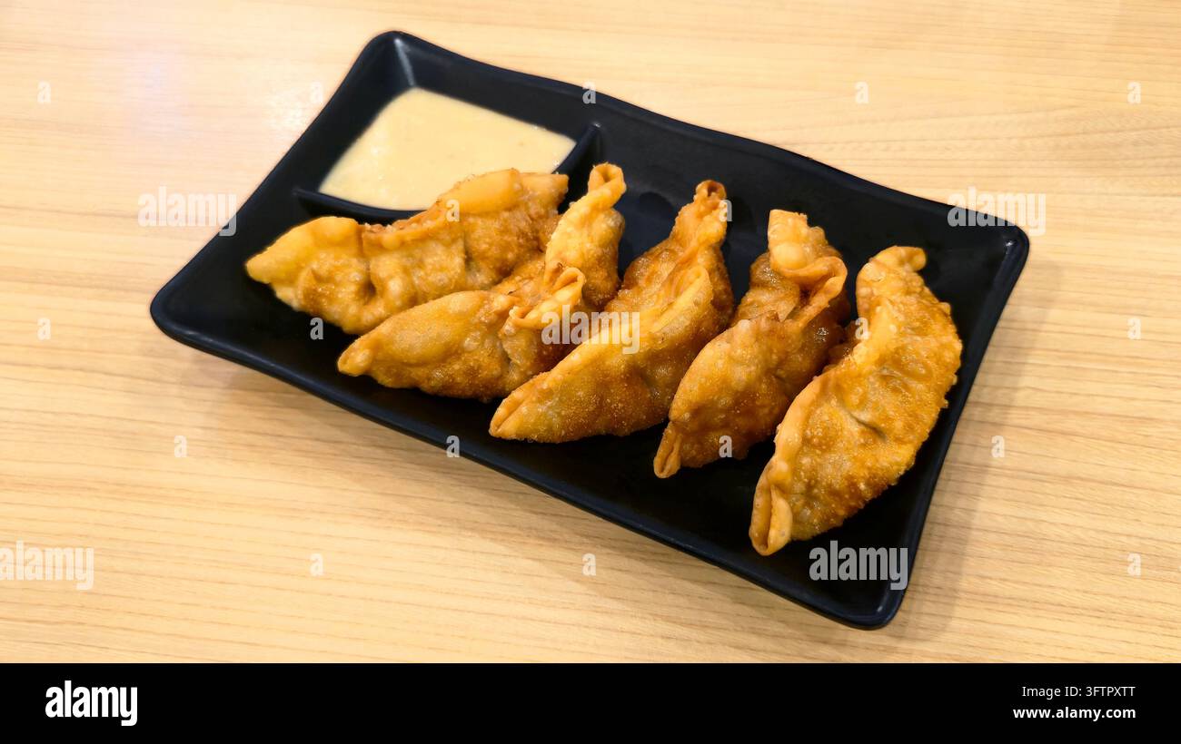 Knusprig gebratene japanische Gyoza-Teigtaschen serviert auf einem schwarzen Teller mit cremiger Dip-Sauce auf einem Holztisch, beliebte asiatische Vorspeise und Snack. - Smartphone-aufgenommenes Stockfoto