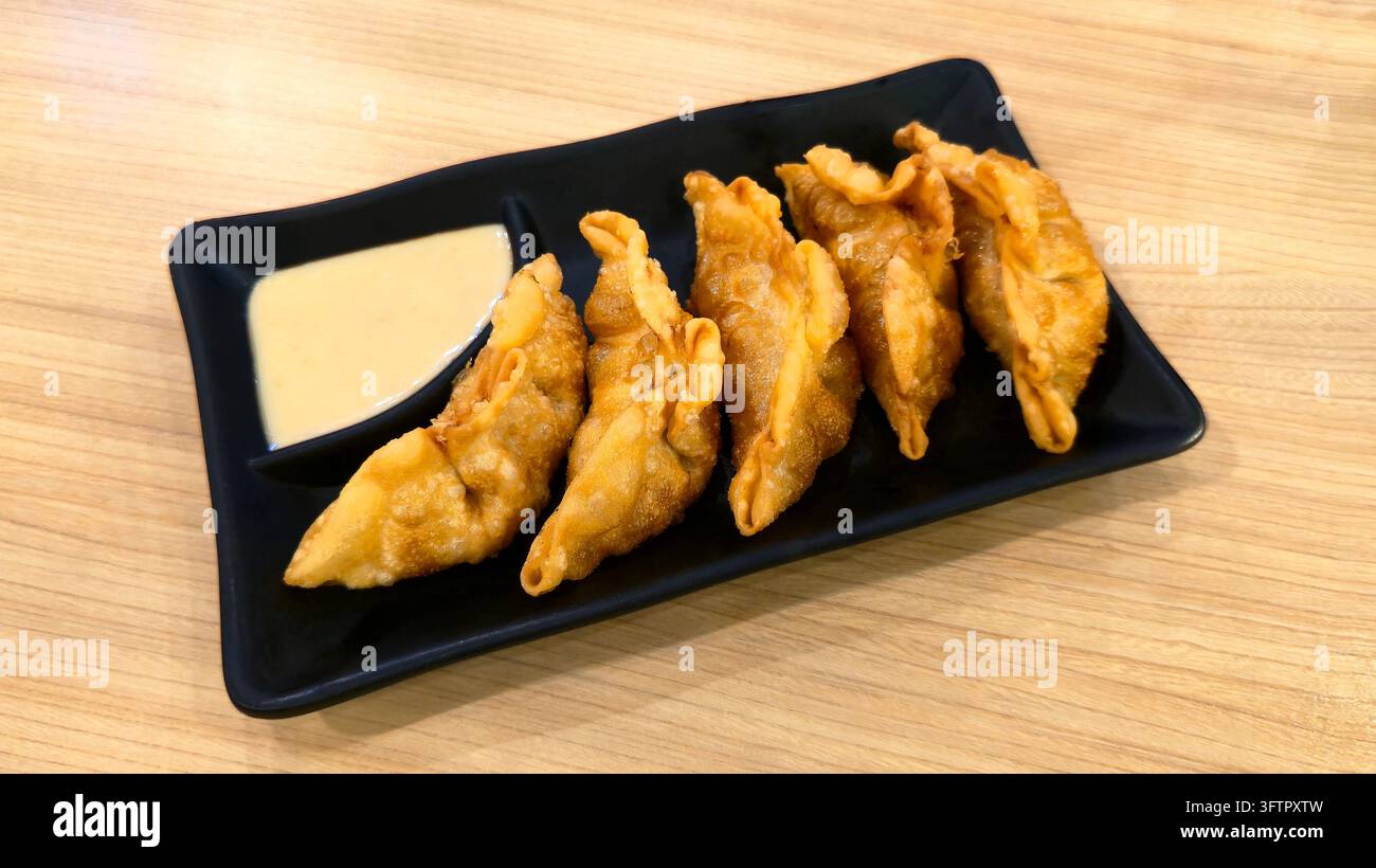 Knusprig gebratene japanische Gyoza-Teigtaschen serviert auf einem schwarzen Teller mit cremiger Dip-Sauce auf einem Holztisch, beliebte asiatische Vorspeise und Snack. - Smartphone-aufgenommenes Stockfoto