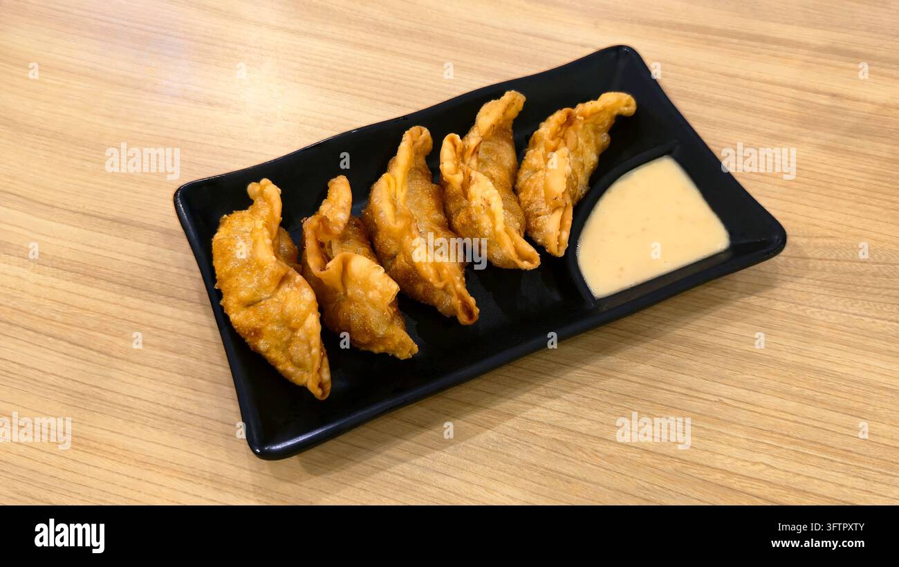 Knusprig gebratene japanische Gyoza-Teigtaschen serviert auf einem schwarzen Teller mit cremiger Dip-Sauce auf einem Holztisch, beliebte asiatische Vorspeise und Snack. - Smartphone-aufgenommenes Stockfoto