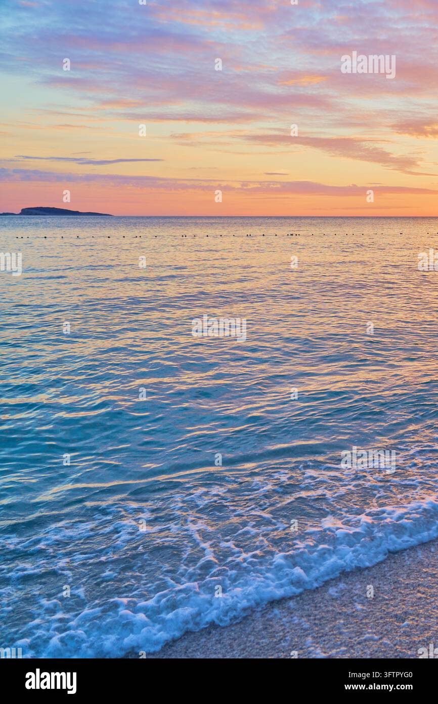 Pastellfarbener mediterraner Sonnenuntergang über ruhigem Meer mit sanften Wellen und lebhaftem Abendhimmel. Stockfoto