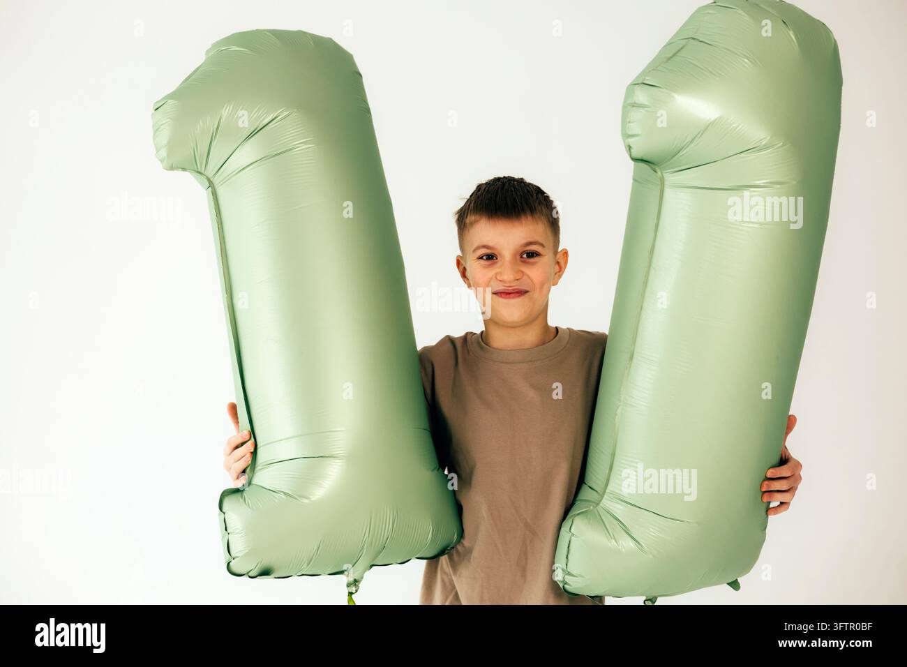 Zufriedener 11-jähriger Junge hält grüne Luftballons mit der Nummer 11 Stockfoto