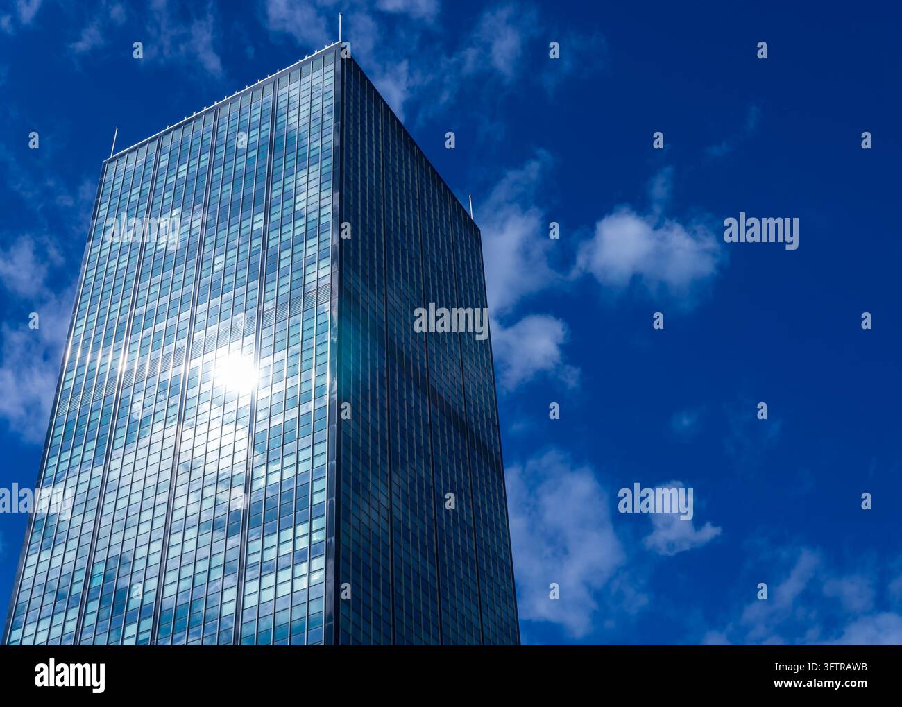 Niedrigwinkelaufnahme des Treptowers-Büroturms in Berlin Alt-Treptow, wobei das helle Sonnenlicht auf seiner Glasfassade reflektiert wird vor einem blauen, bewölkten Himmel. Stockfoto