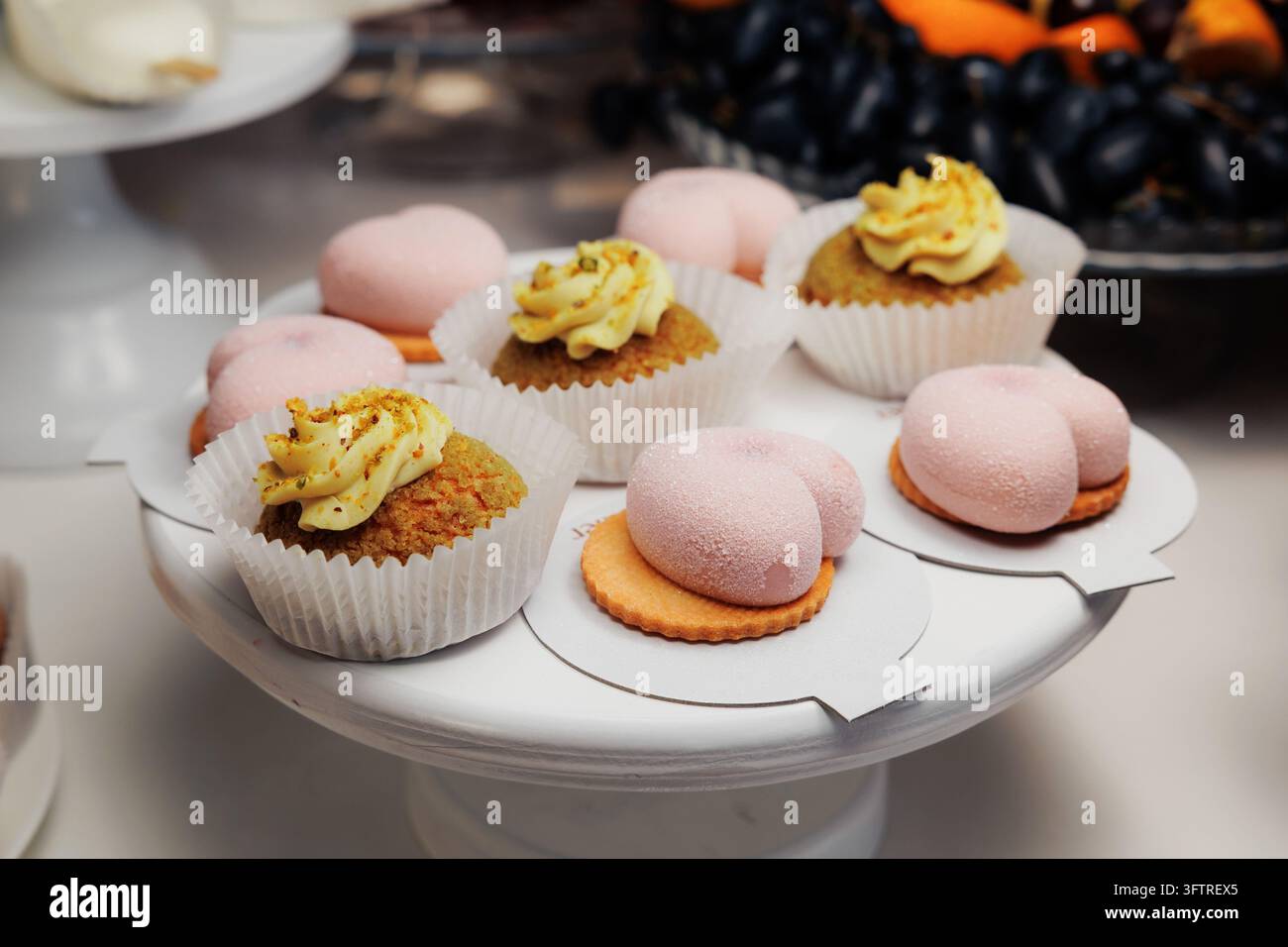 Nahaufnahme von verschiedenen Gebäckstücken auf weißem Kuchenständer, darunter Pistazien-Cupcakes mit gelber Creme in Papierförmchen und rosa zuckerbeschichtet Stockfoto