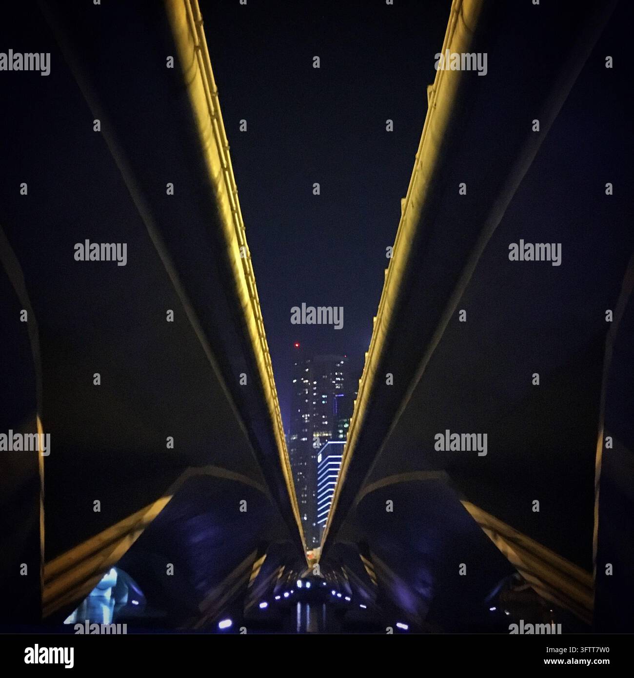 Ein Nachtblick schaut nach oben durch die massiven Strukturträger einer modernen Brücke oder eines Turms, deren dunkle Formen sich um eine schmale Öffnung sammeln Stockfoto