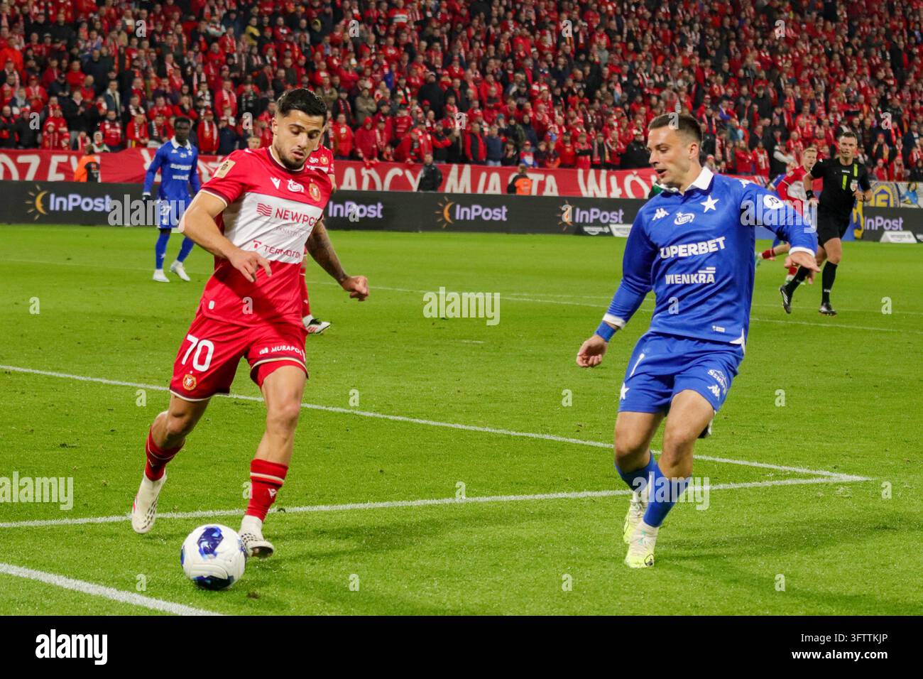 Lódź, Polen – 16. Oktober 2026: Polnisches Ekstraklasa-Fußballspiel zwischen Widzew Łódź und Wisła Kraków im Widzew-Stadion. Spielaction mit einem Widzew-Spieler mit Ball in rotem Trikot und einem Wisła-Spieler in blauem Trikot, die auf dem Spielfeld vor begeisterten Fans auf den Tribünen konkurrieren. Stockfoto