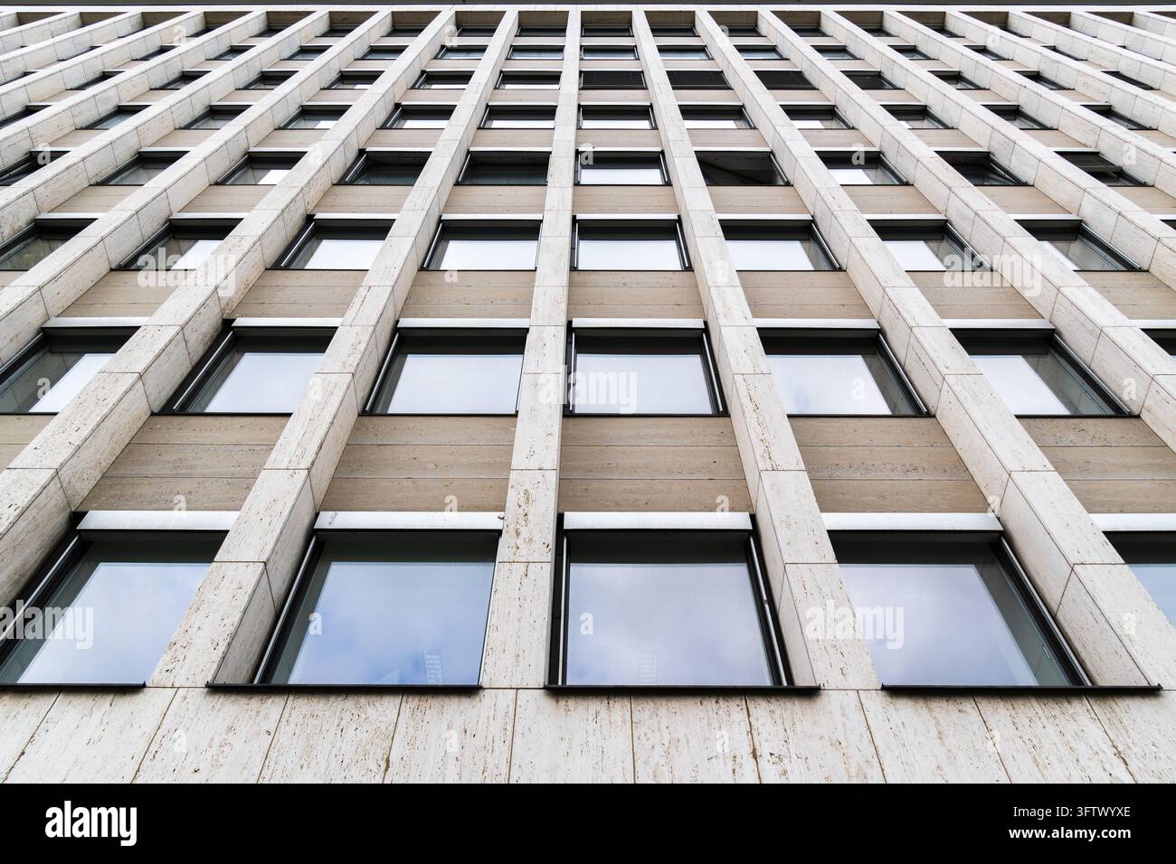 Schmale Fenster unterbrechen die helle Steinverkleidung eines Bürogebäudes. Wiederholte vertikale Elemente und versetzte Fensterpositionen erzeugen eine geometrische Stockfoto