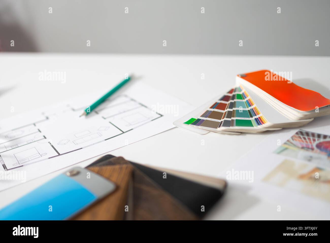 Ein Designerstudio zeigt einen diagonalen Grundriss und einen Farbfächer, mit Furnierproben und einem grünen Bleistift, der Ruhe signalisiert Stockfoto