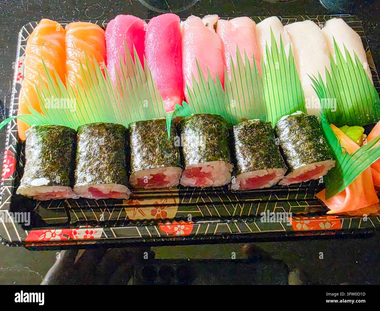 Farbenfrohes Takeaway-Sushi-Set bestehend aus Nigiri und Maki in einer Plastikbox, dekoriert mit grünem Plastik-„Gras“ Stockfoto