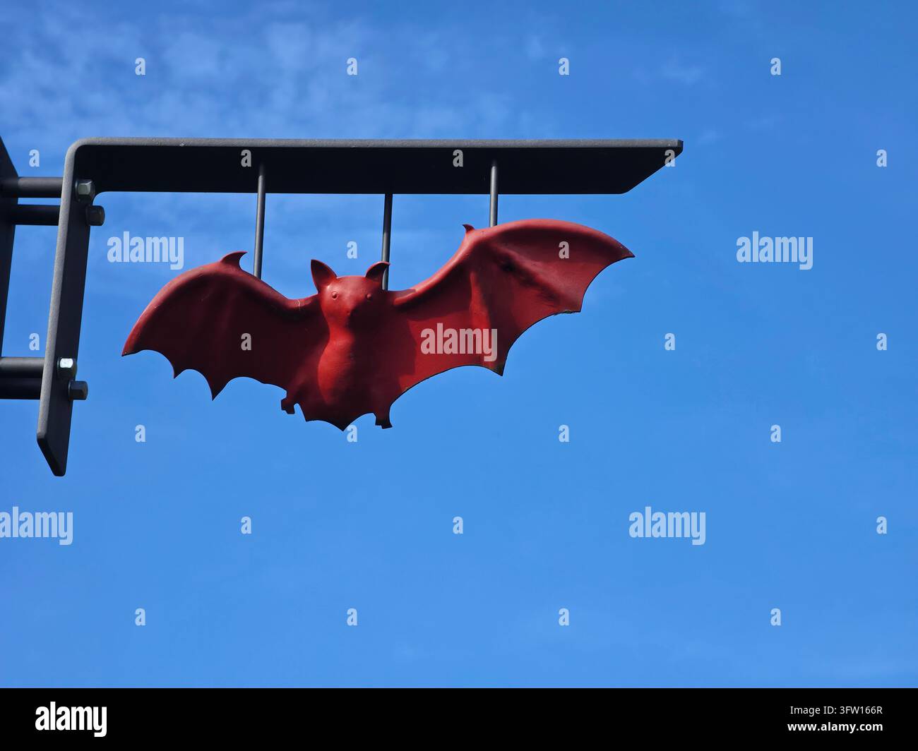 Rote dekorative Fledermausfigur, die an einer Metallhalterung hängt, Blick von unten unter klarem blauem Himmel - Smartphone-aufgenommenes Stockfoto