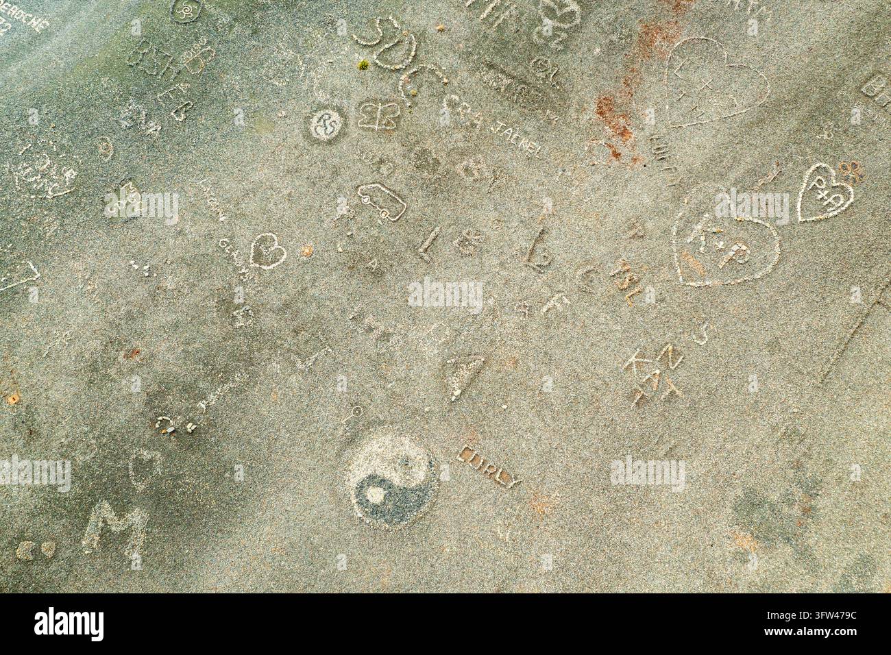 Eingravierte Initialen, Namen, Herzen und kleine Zeichnungen bedecken eine verwitterte Steinoberfläche am Strand von Nonza. Stockfoto